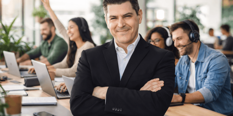 Formateur en costume noir, bras croisés, devant des participants joyeux pendant une journée de formation à distance sur les Agents Copilot (Copilot Studio).